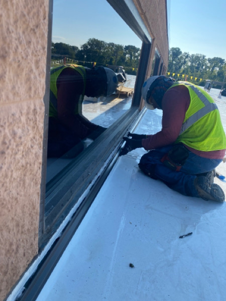 roofer working on a section of commercial roofing next to a window.